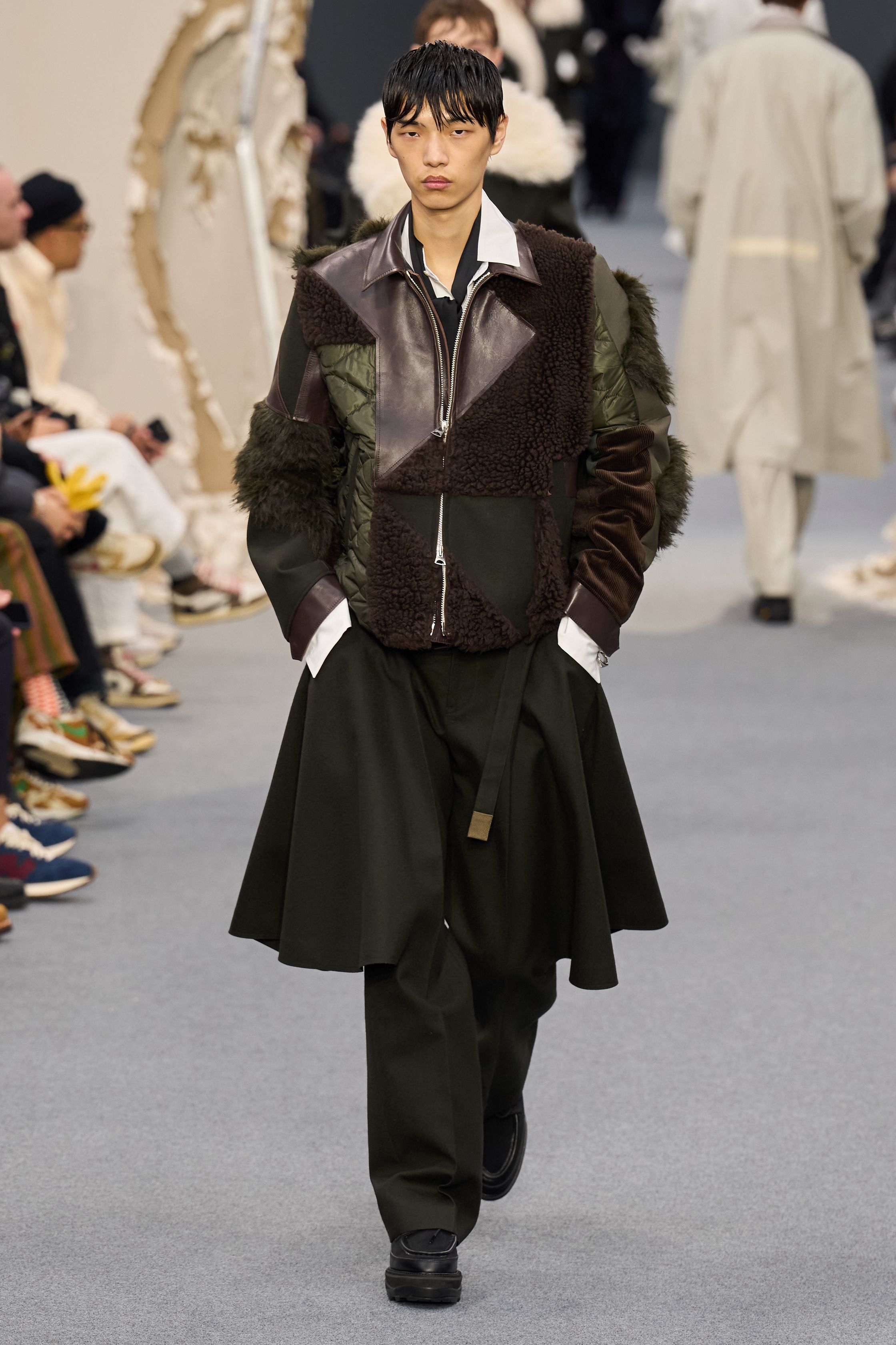 Sacai 2026秋冬再次展示其无可复制的“混合美学”。正装、牛仔、皮草与制服元素被高度结构化地拼接，形成既熟悉又陌生的服装形态。性别边界被进一步模糊，层叠结构制造流动节奏，使行走本身成为设计的一部分。系列在秩序与混乱之间找到平衡，是Sacai 对当代复杂生活状态的持续回应-顽石频道趋势研究